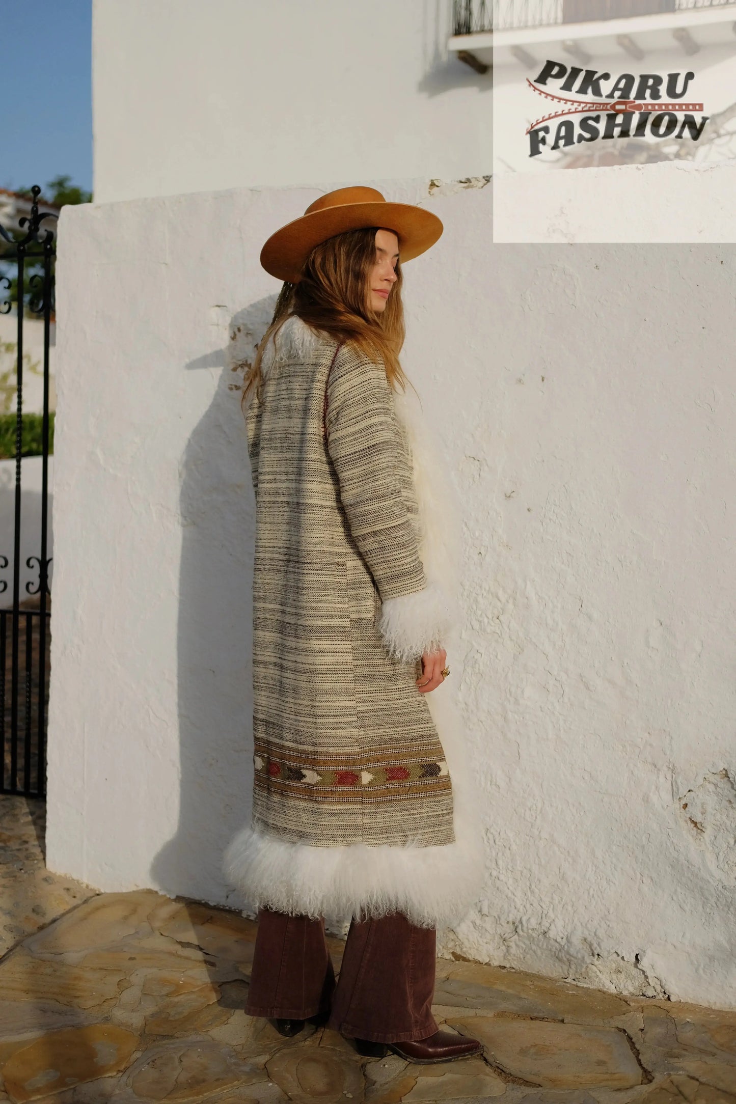 Side view of a woman in a boho fur trim long coat with soft fur details and a wide-brim hat