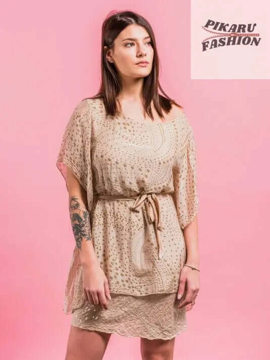 Woman in beige puff sleeve dress with waist tie, standing against pink background