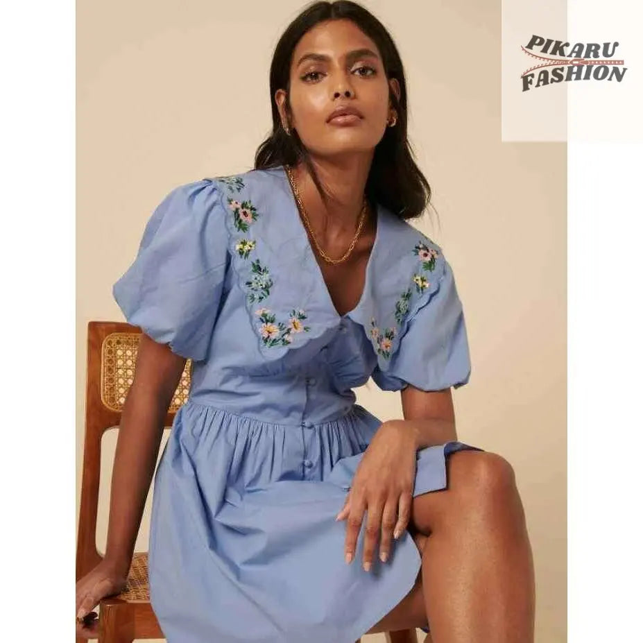 Woman in light blue puff sleeve dress with floral embroidery sitting on wooden chair