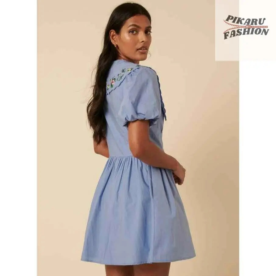 Woman in light blue short puff sleeve dress with floral embroidery on back collar