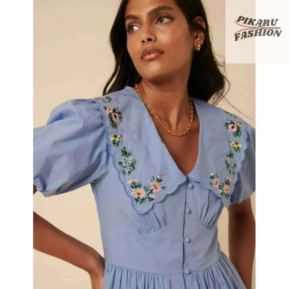 Woman wearing a light blue puff sleeve dress with floral embroidery on the collar