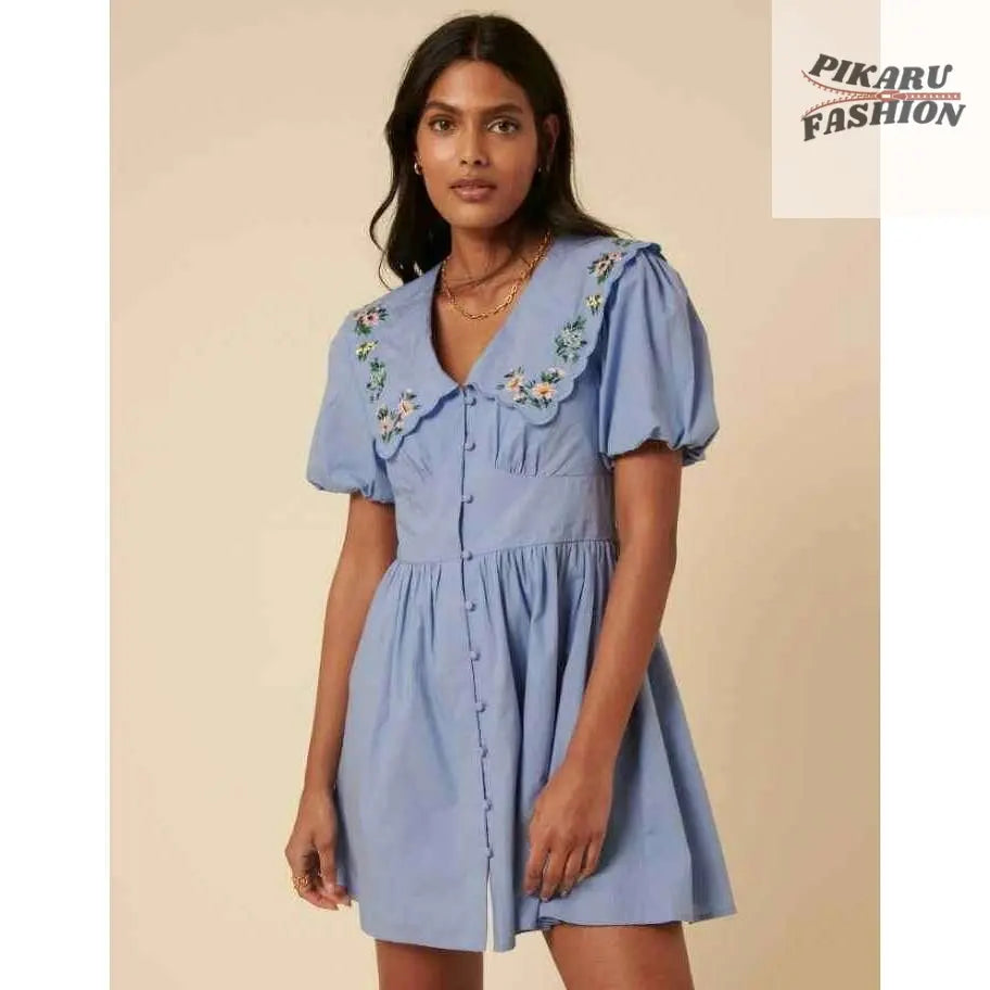 Woman wearing light blue short dress with puff sleeves and floral embroidered collar