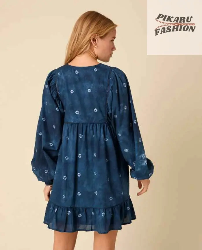 Woman wearing blue floral long sleeve dress with ruffle hem, seen from the back