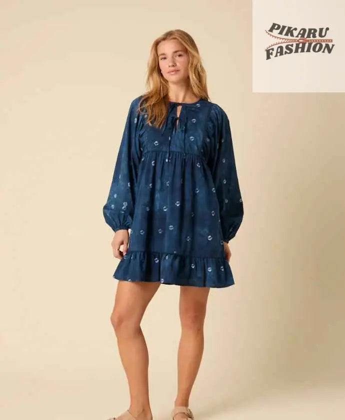 Woman in blue long sleeve mini dress with floral print standing in studio
