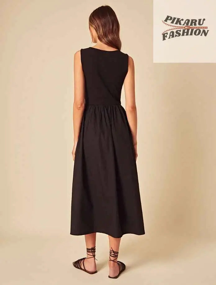 Woman in sleeveless black midi dress and sandals standing against neutral background