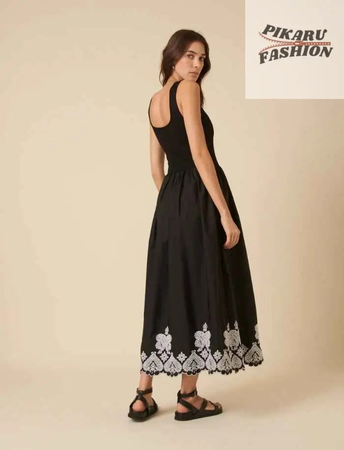 Woman modeling black sleeveless midi dress with white embroidered hem, neutral background