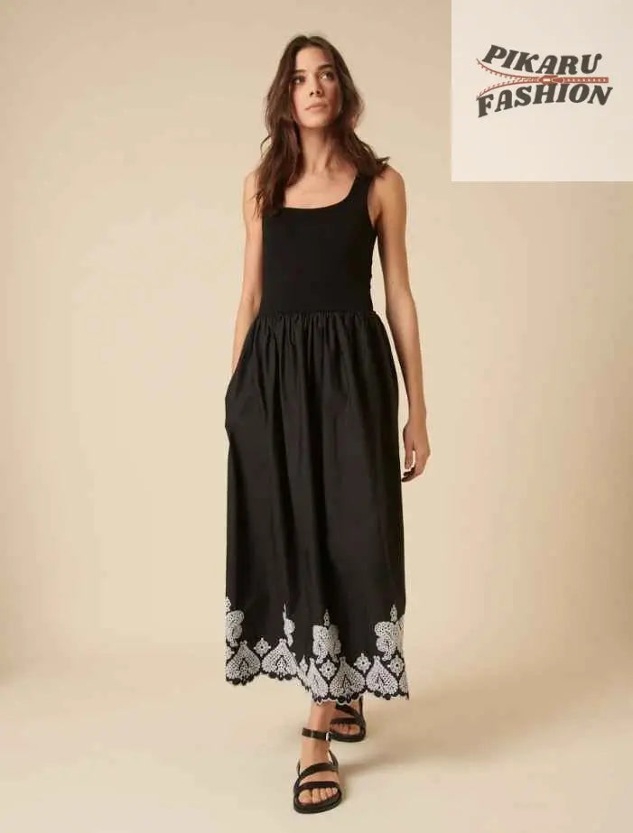 Woman in sleeveless black midi dress with white floral hem embroidery, standing indoors