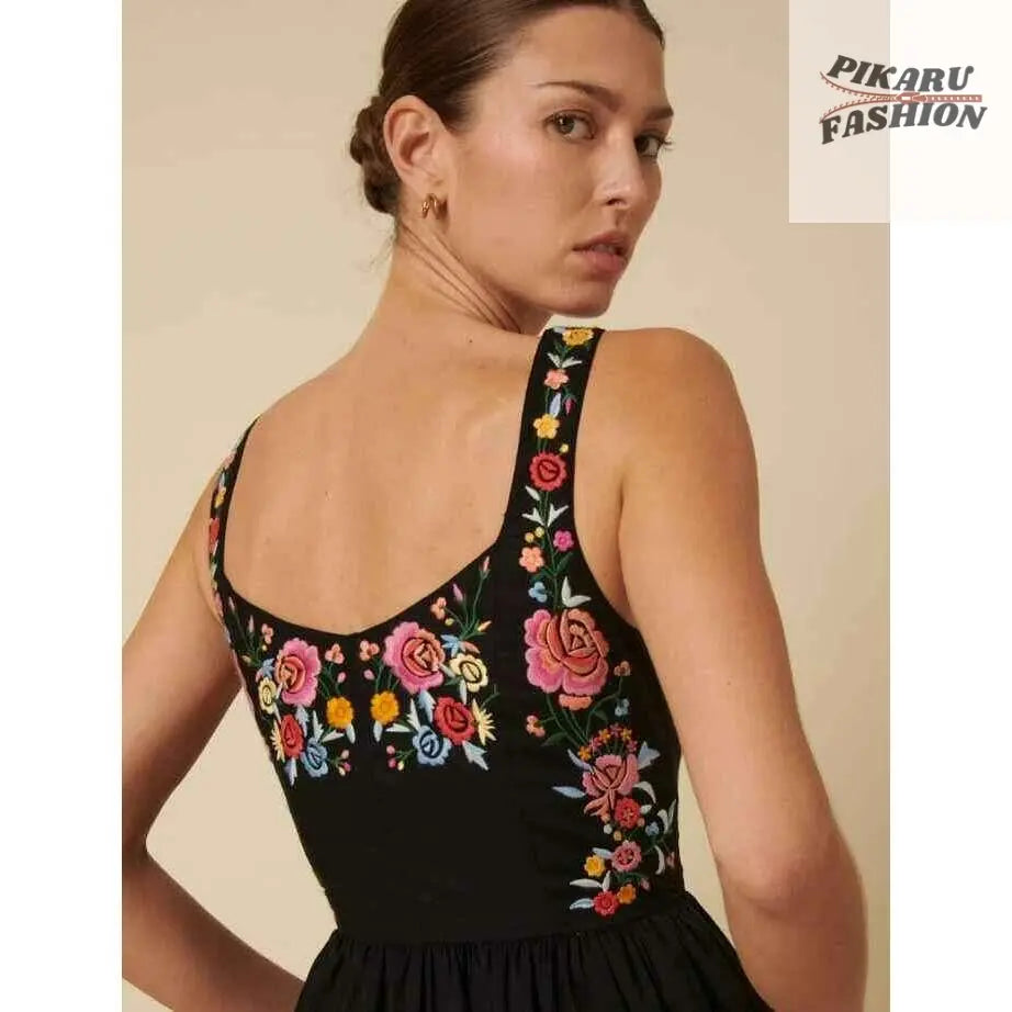 Woman in black sleeveless dress with colorful floral embroidery, looking over shoulder