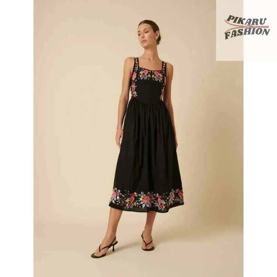 Woman wearing a black midi dress with colorful floral embroidery on bodice and hem