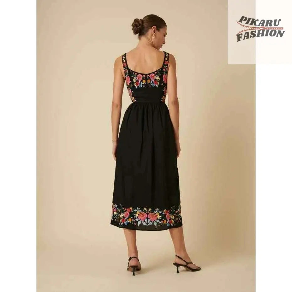 Woman in black sleeveless midi dress with colorful floral embroidery on back and hem