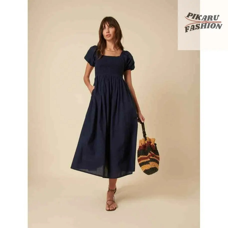 Woman in puff sleeve navy midi dress with square neckline holding a colorful woven bag