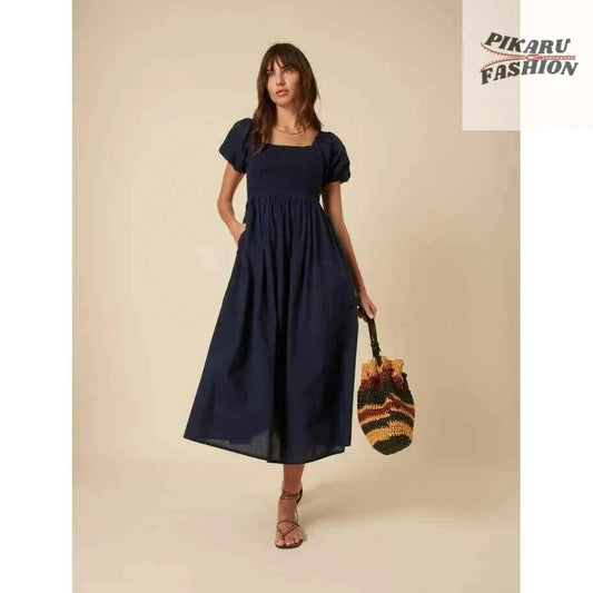 Woman in puff sleeve navy midi dress with square neckline holding a colorful woven bag