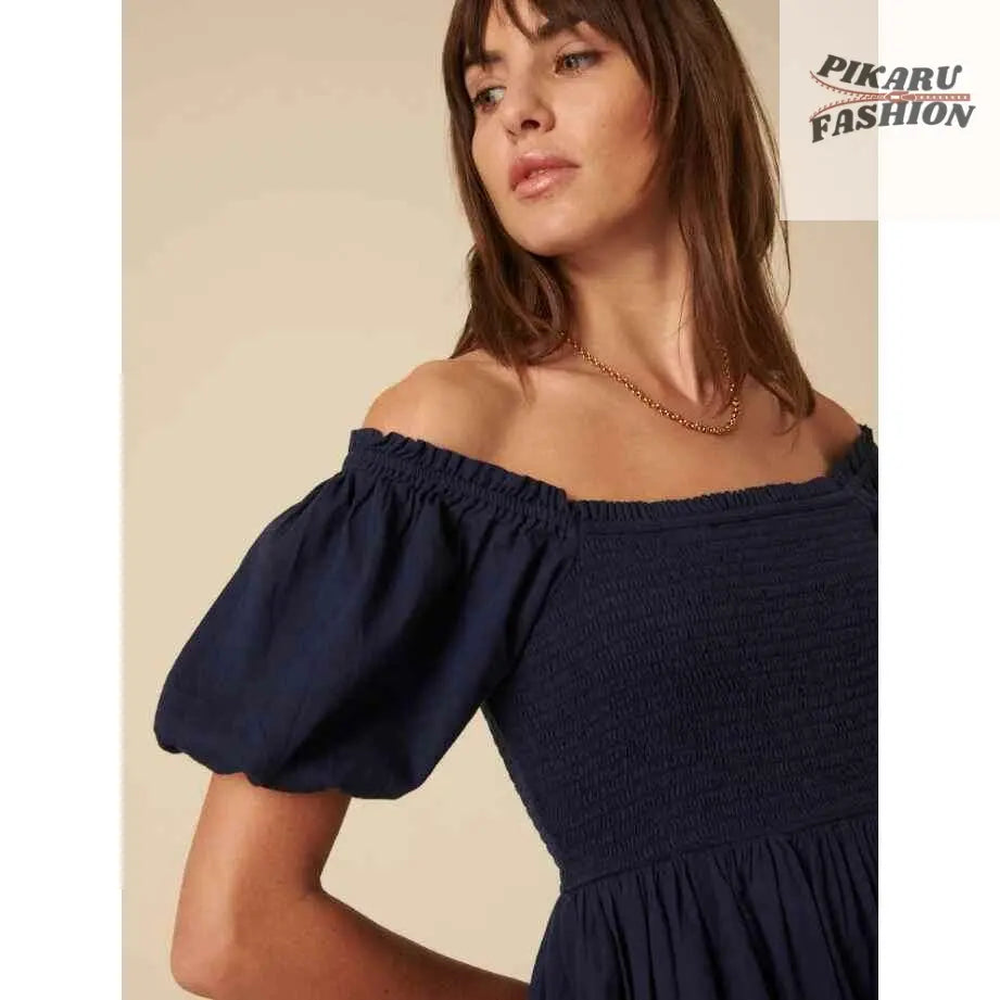 Woman wearing navy off-shoulder puff sleeve dress with gold chain necklace