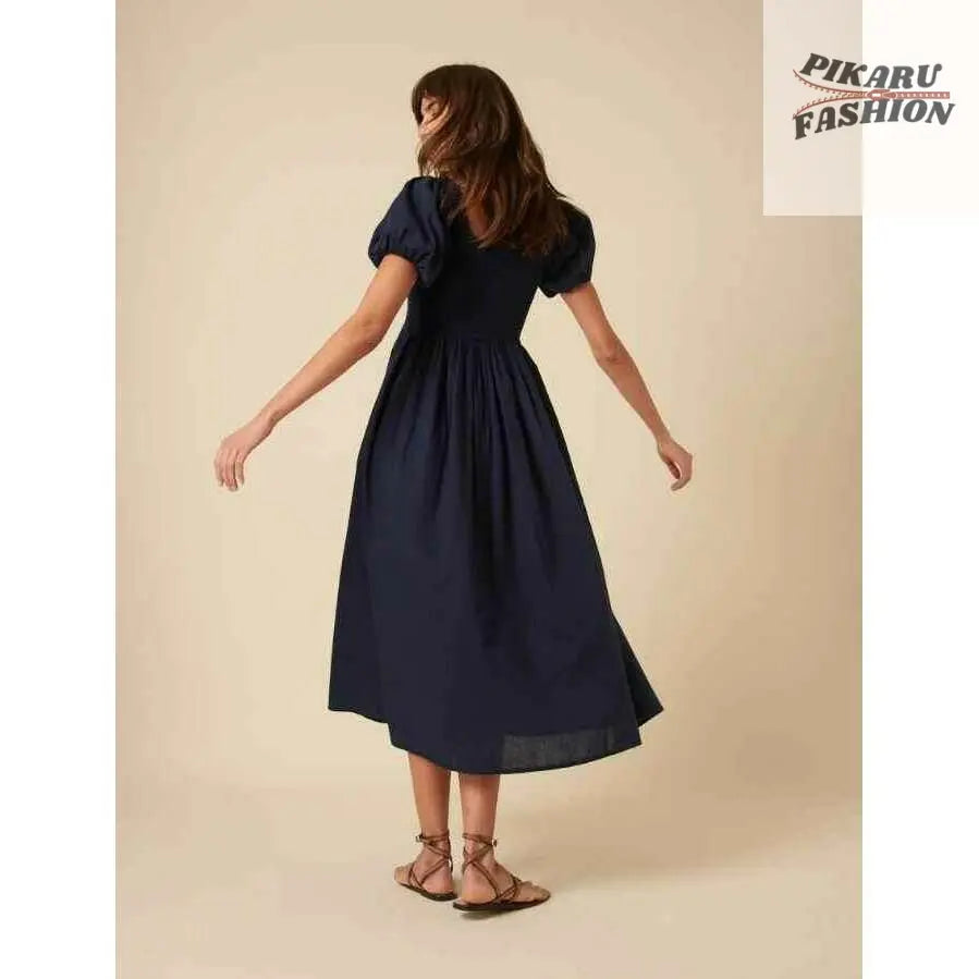 Woman in navy puff sleeve midi dress and sandals standing against beige background