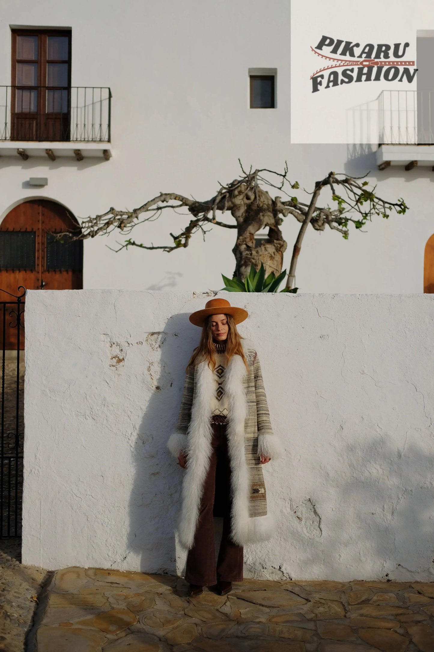 Front view of a woman wearing a boho fur trim long coat styled with brown pants and a hat