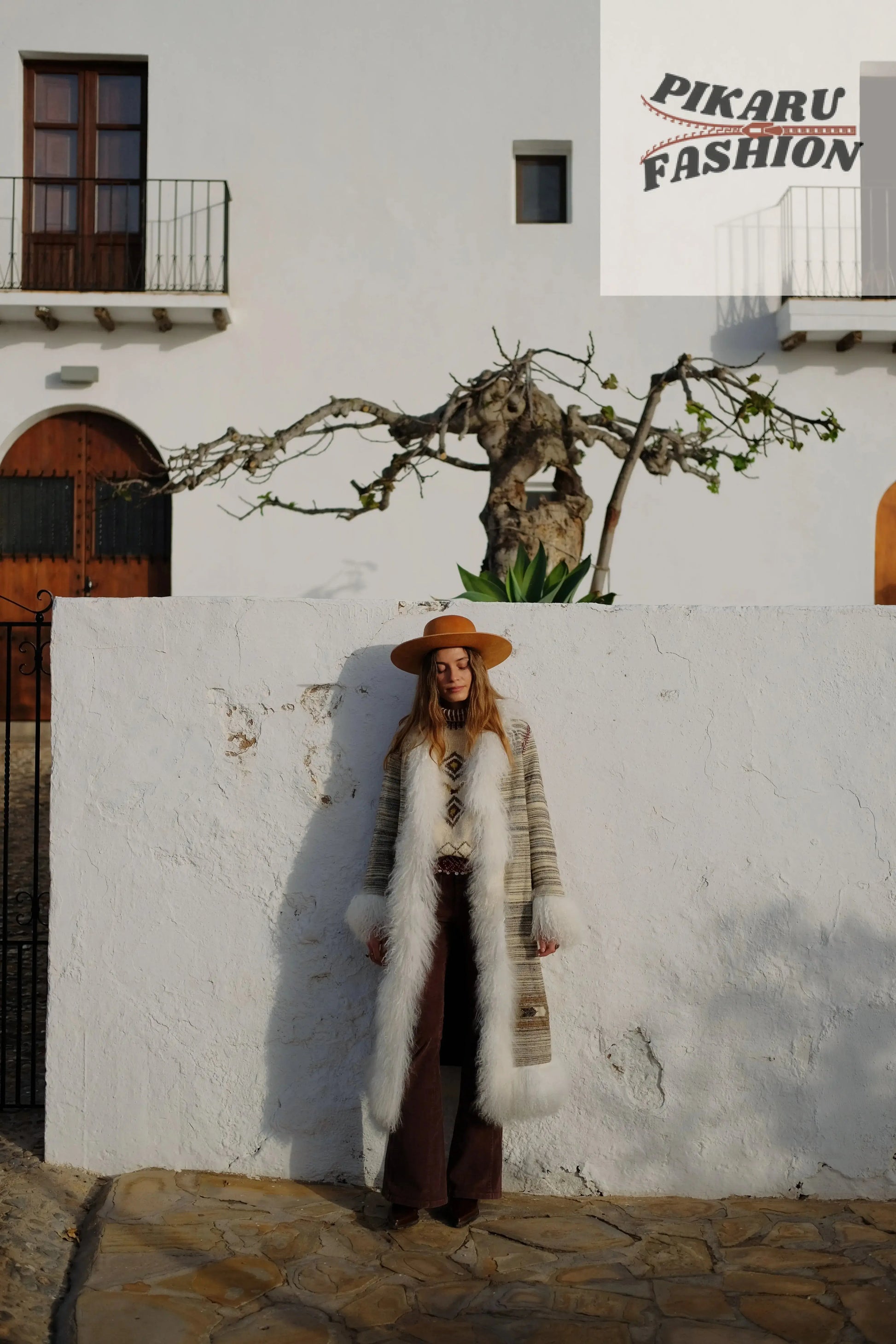 Front view of a woman wearing a boho fur trim long coat styled with brown pants and a hat